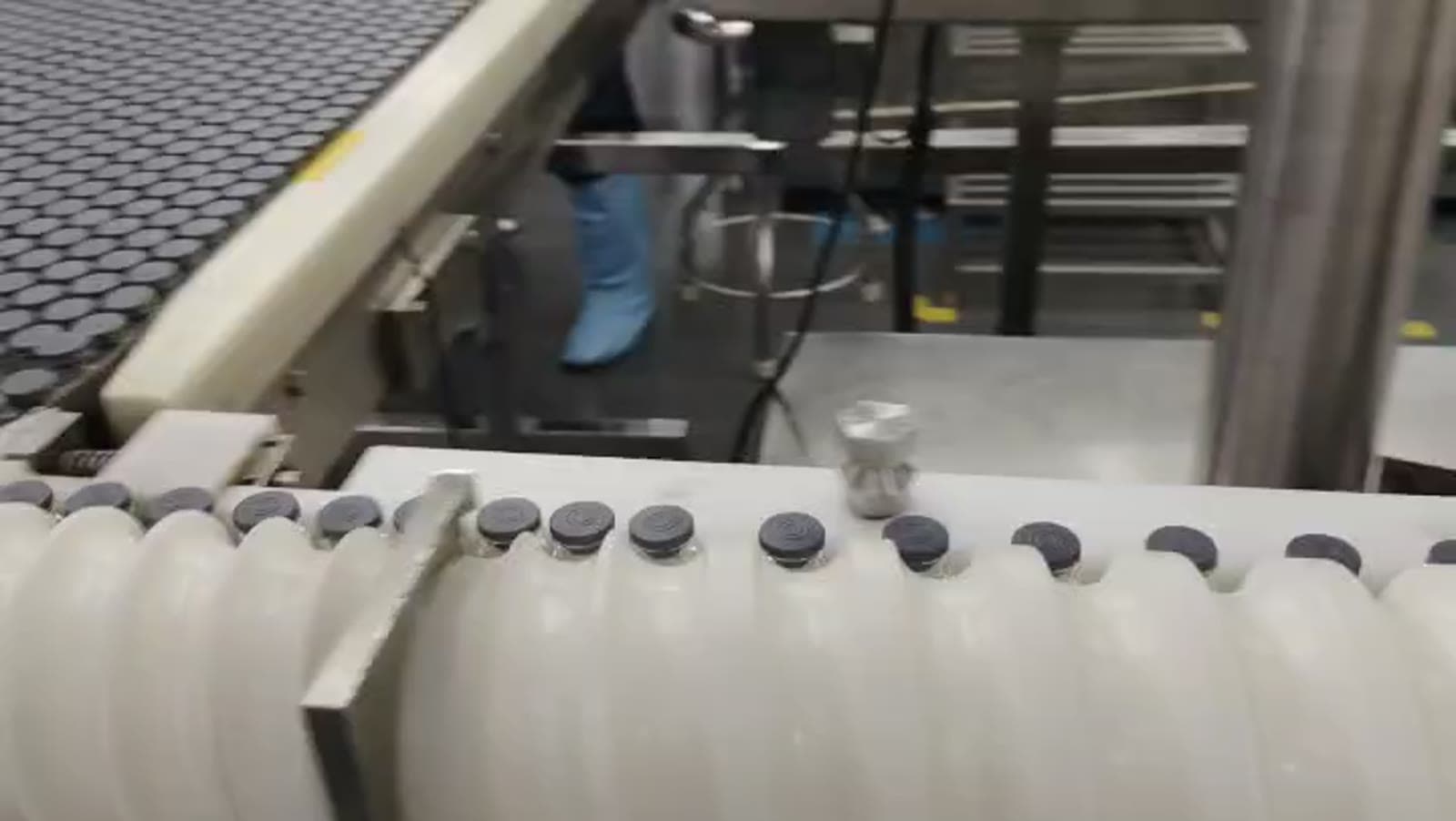 PeptideXpo vial-filling line in active production, vials moving along the conveyor with operator in cleanroom PPE in the background