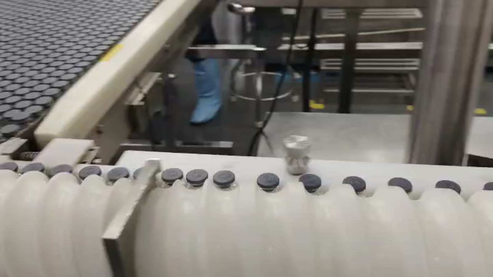 PeptideXpo vial-filling line in active production — vials moving along the conveyor with operator in cleanroom PPE in the background